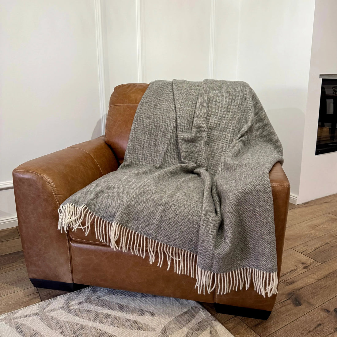 Pătură gri din lână naturală, așezată pe fotoliu maro