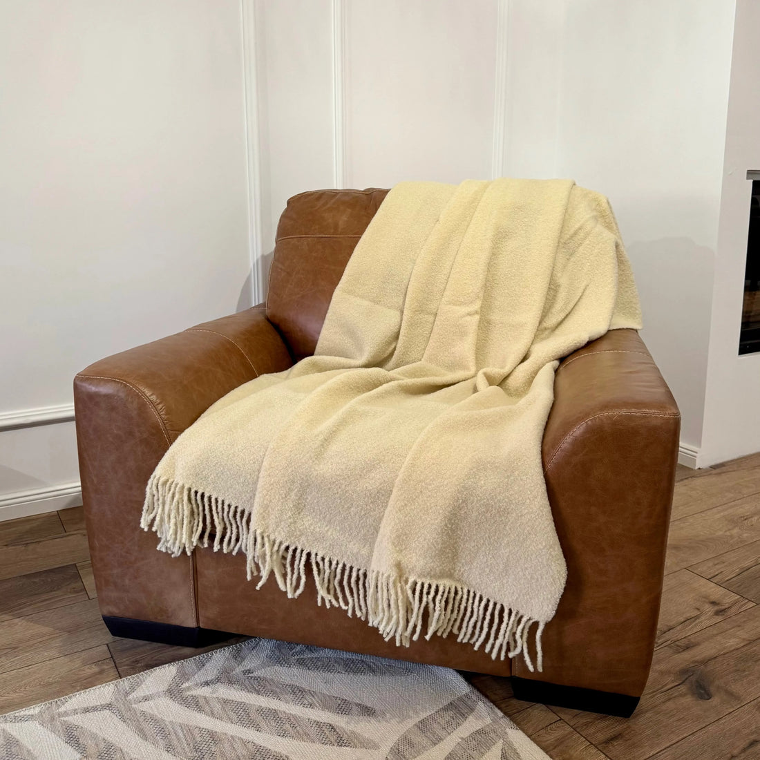 Pătură albă bouclé moale, elegant așezată pe un fotoliu din piele