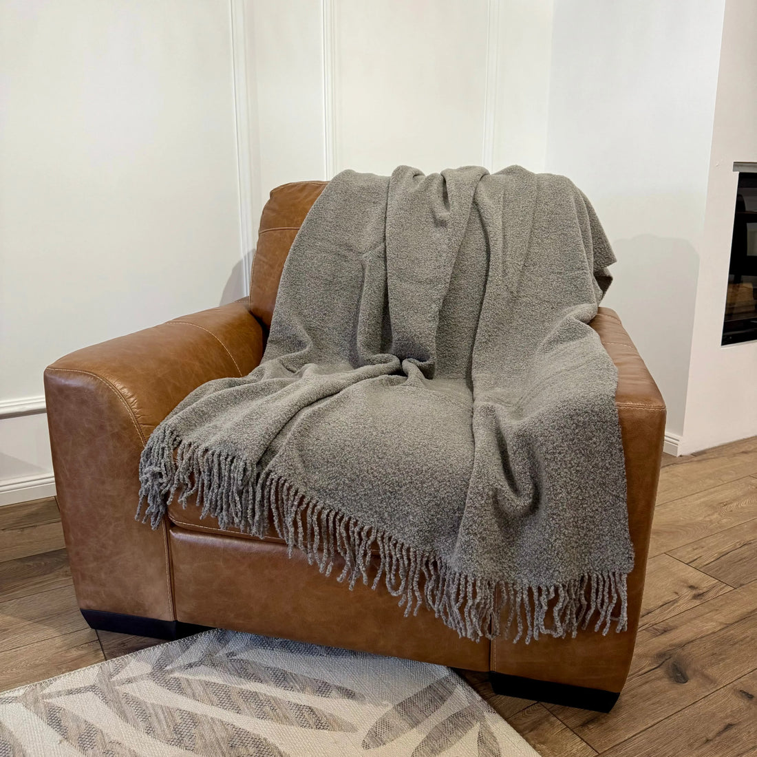 Pătură gri cu textură bouclé, elegant așezată pe fotoliu maro