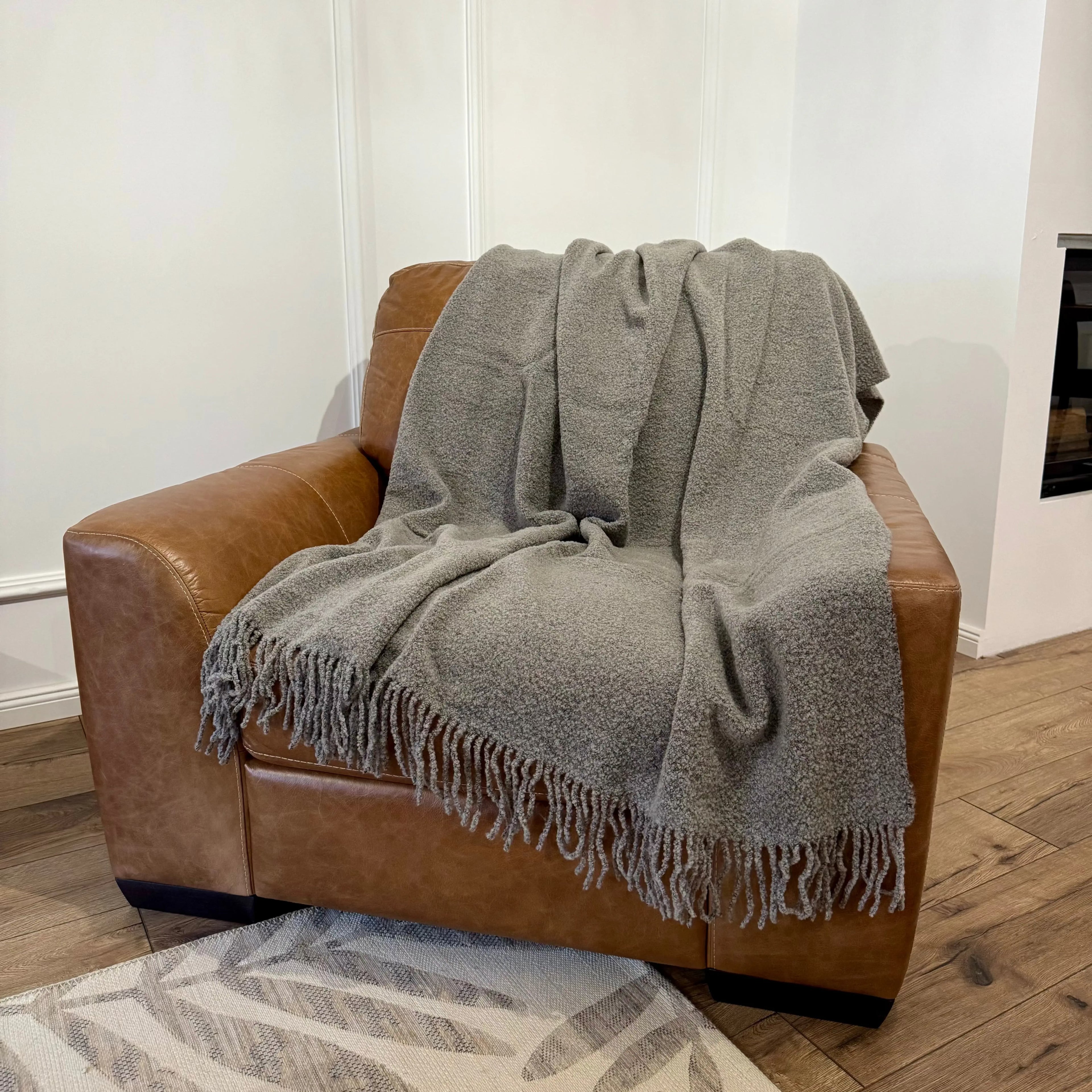 Pătură gri cu textură bouclé, elegant așezată pe fotoliu maro
