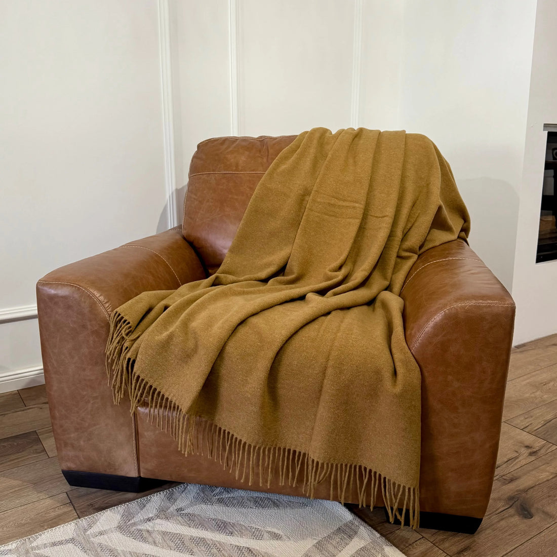 Pătură din lână merino în nuanță camel, plasată pe fotoliu din piele
