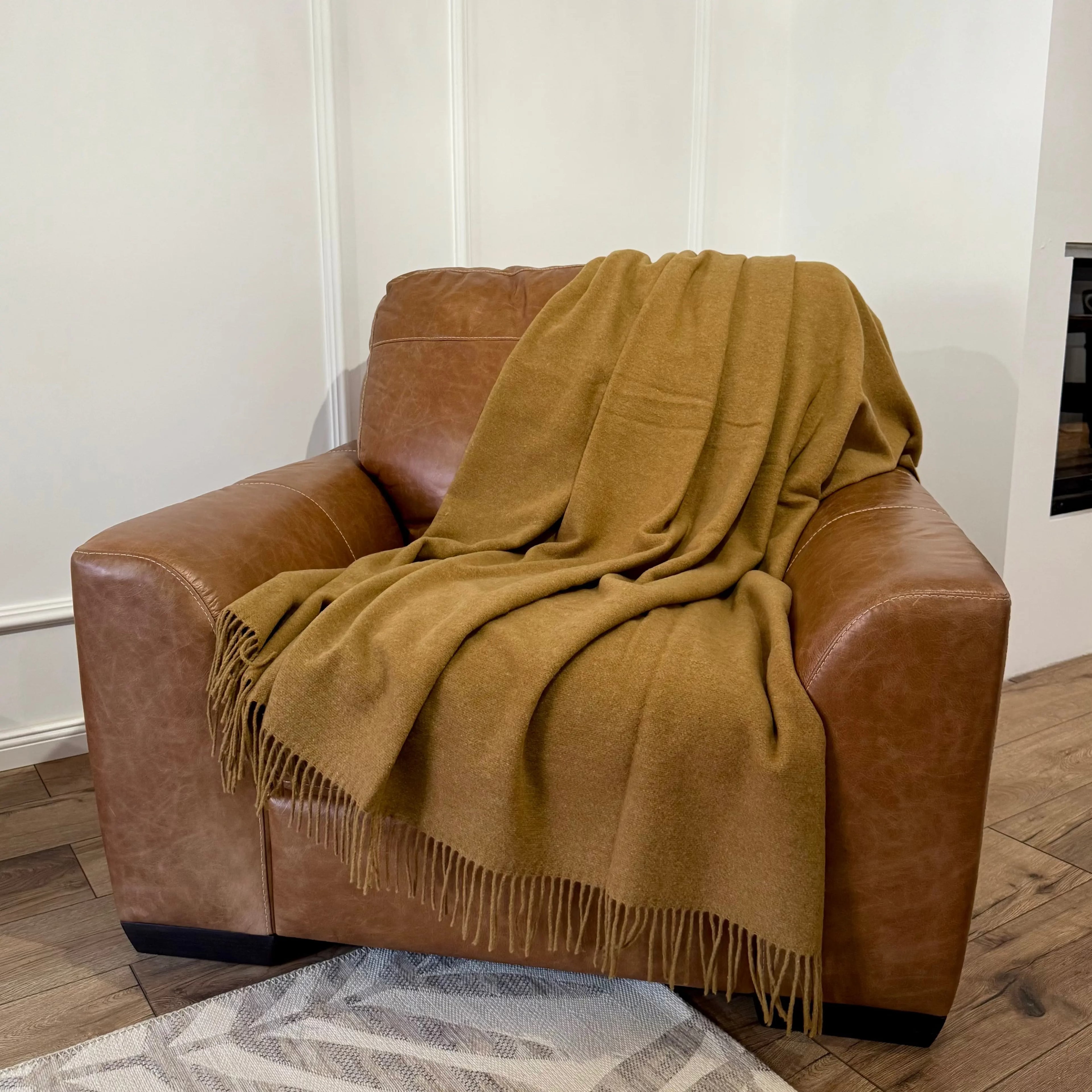 Pătură din lână merino în nuanță camel, plasată pe fotoliu din piele
