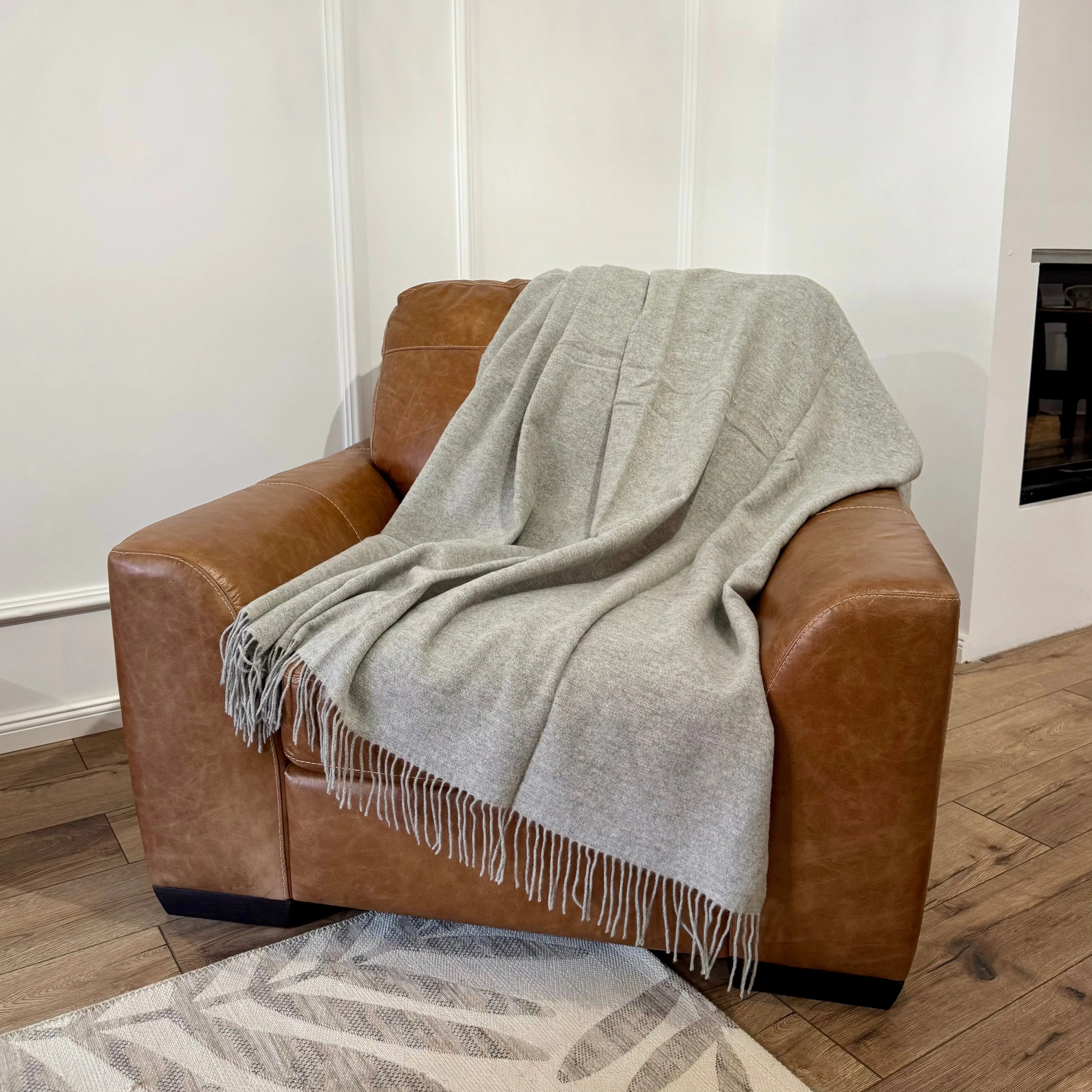 Pătură gri deschis MERINO din lână merino, întinsă pe fotoliu din piele